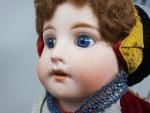 Une poupée à tête de porcelaine, yeux bleus fixes, bouche...